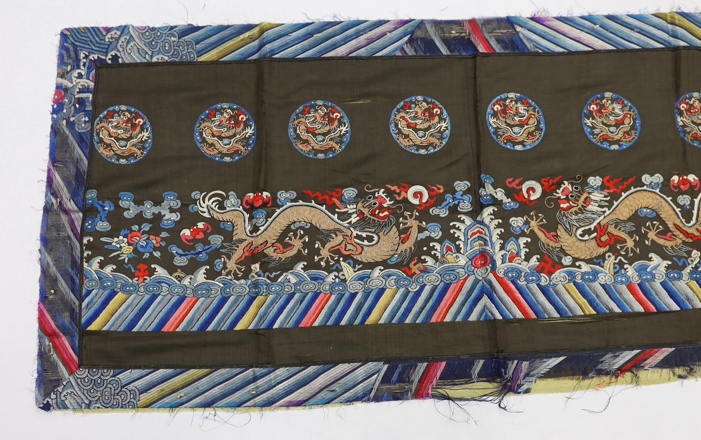 A Chinese polychrome silk and gold thread embroidery on a black silk background, possibly from the lower section of a robe, depicting dragons and auspicious symbolic motifs, 130cm long x 59cm high